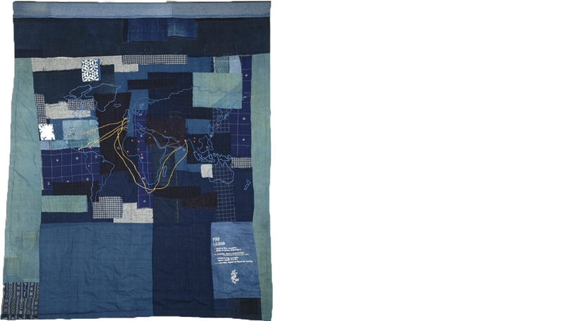A quilt made of indigo (blue) dyed fabrics. On the quilt, is a sewn map with yellow string.